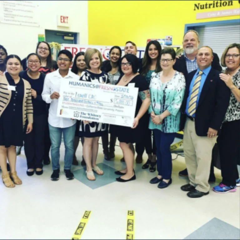 group of people in colorful room holding large check
